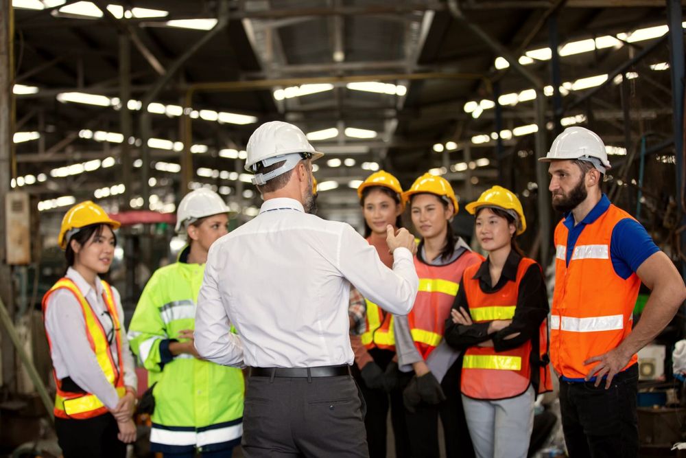 Supervisor da una charla de seguridad a un grupo de trabajadores con casco y chaleco