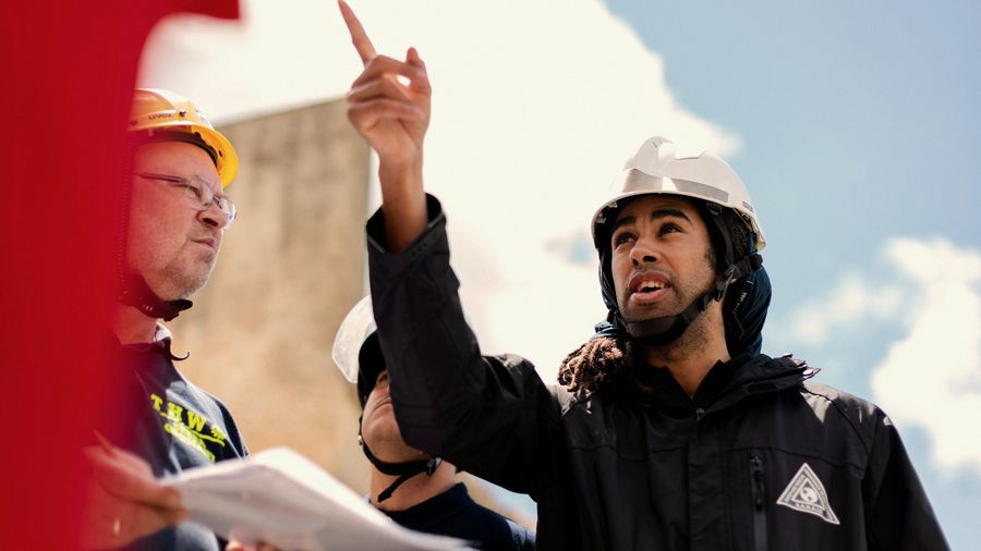 Supervisor con casco señala un punto de la obra mientras conversa con su equipo
