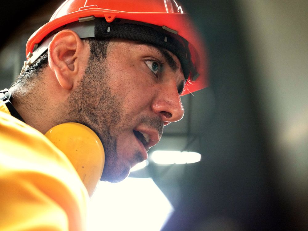 Trabajador con casco rojo y protectores auditivos observa con atención su área de trabajo